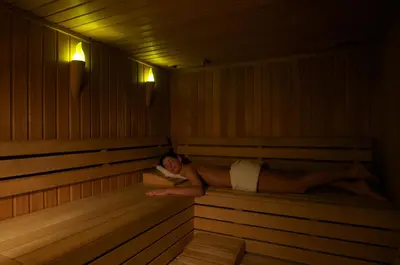 a woman laying in a sauna with a book at Hotel Lovec in Bled