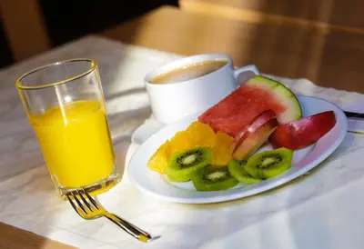 a plate of fruit and a cup of orange juice at Hotel Tabor Maribor in Maribor