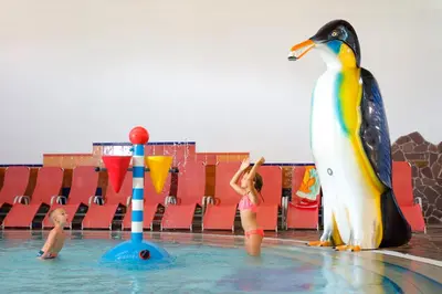 a little girl standing in the water next to a penguin at Terme Zrece - Hotel Vital in Zreče
