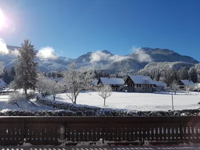 a snow covered yard with a house and mountains at Hotel Gasperin Bohinj in Bohinj