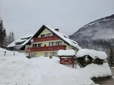 a snow covered house with a sign in front of it at Apartments Bohinj Mavrica in Bohinj