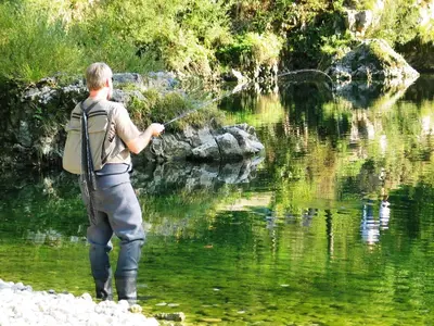 a man is standing in the water fishing at Apartments Bohinj Mavrica in Bohinj