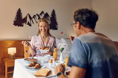 a woman sitting at a table with a man eating food at Pohorje Village Wellbeing Resort - Wellness & Spa Hotel Bolfenk in Pohorje