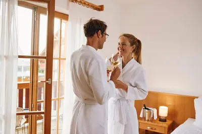 a man and woman standing in a hotel room drinking champagne at Pohorje Village Wellbeing Resort - Wellness & Spa Hotel Bolfenk in Pohorje