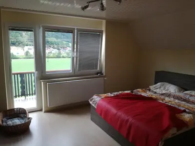 a bedroom with a bed with a red blanket and two windows at Poldas apartments in Poljane nad Škofjo Loko