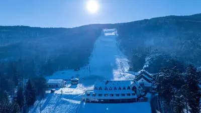 a snow covered slope with a building and a mountain at Hotel Arena Maribor in Maribor