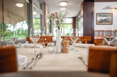 a table with wine glasses and a vase with flowers at Hotel Dvor Jezersek Brnik in Cerklje na Gorenjskem
