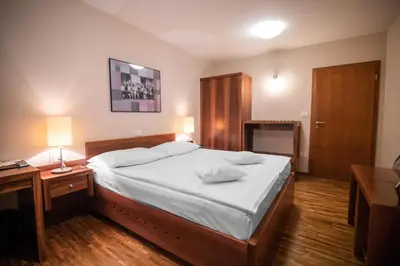 a bedroom with a large bed with white sheets and wooden floors at Hotel Dvor Jezersek Brnik in Cerklje na Gorenjskem