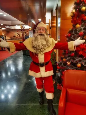 a man dressed as santa claus standing next to a christmas tree at Hotel Kompas in Kranjska Gora