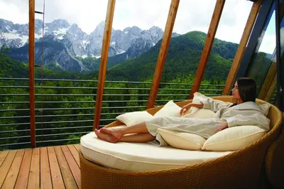 a woman laying in a wicker chair on a balcony at Hotel Špik in Kranjska Gora