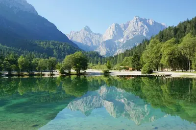 a lake with trees and mountains in the background at Vitranc Apartments in Kranjska Gora