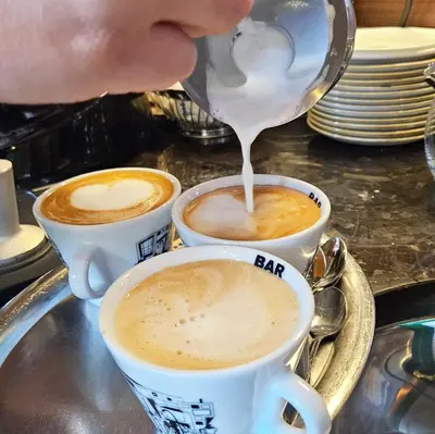 a person pouring milk into two cups of coffee at Sabotin, Hotel & Restaurant in Nova Gorica