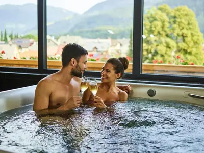 a man and woman sitting in a bath tub with wine glasses at Korona, Resort & Entertainment in Kranjska Gora