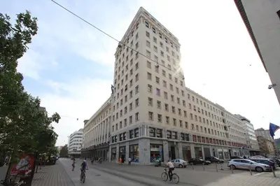 a large white building on a city street with people riding bikes at Skyscraper Apartment Tour As Ljubljana in Ljubljana