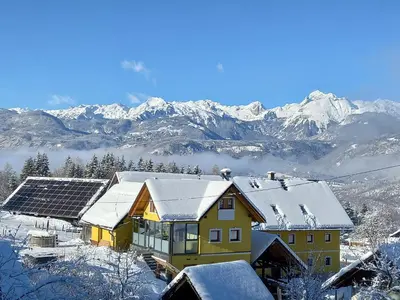 a house with snow on the roof with mountains in the background at Apartments Tubej in Bohinj