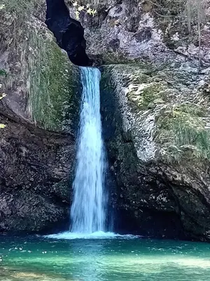 a waterfall on the side of a mountain with green water at Apartments Tubej in Bohinj