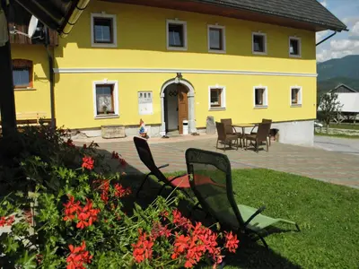 a yellow house with chairs and flowers in the yard at Apartments Tubej in Bohinj