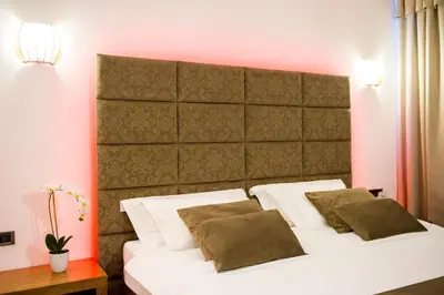 a bedroom with a white bed with a large headboard at Safir Hotel Casino in Sežana