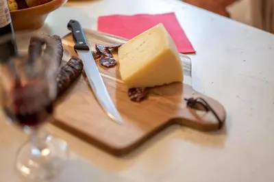 a piece of cheese on a cutting board with a glass of wine at Apartments Trata in Kranjska Gora