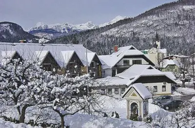 a house covered in snow with mountains in the background at Hotel Tripič, restaurant and pizzeria in Bohinj