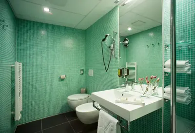 a bathroom with a sink and a toilet and green tiles at Hotel Thermana Park Laško**** Superior in Laško
