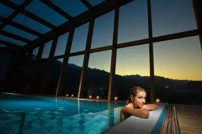 a woman sitting in a swimming pool at sunset at Bohinj Eco Hotel in Bohinj
