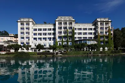 a large white building next to a body of water at Grand Hotel Toplice - Small Luxury Hotels of the World in Bled