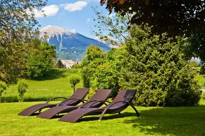 a row of benches sitting in the grass with a mountain at Alp Pension in Bled