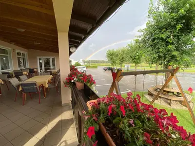 a patio with flowers and a rainbow in the background at Gostisce Golob in Zgornja Polskava