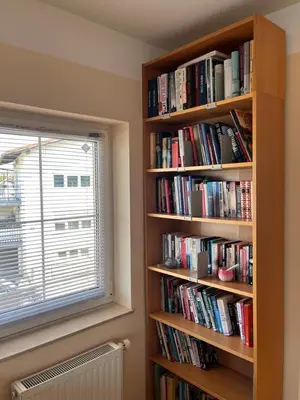 a book shelf filled with books next to a window at Peaceful 4-room house in Maribor - ski friendly in Maribor