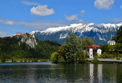 a house on a island in a lake with a snow covered mountain at Adora Luxury Hotel in Bled