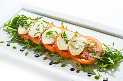 a plate of food with tomatoes and greens at Postojna Cave Rooms & Apartments Proteus in Postojna
