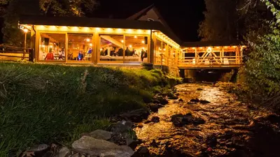 a building with lights on it next to a stream at Gorska Reka Guesthouse in Zreče