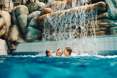 three people in a swimming pool with a waterfall at Apartments Čatež - Terme Čatež in Čatež ob Savi