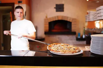 a man holding a pizza on top of a counter at Hotel Marinšek in Naklo