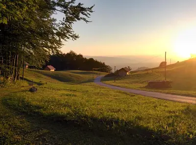 a road on a grassy hill with the sun setting at Tourist Farm Pr'Dovar in Cerklje na Gorenjskem