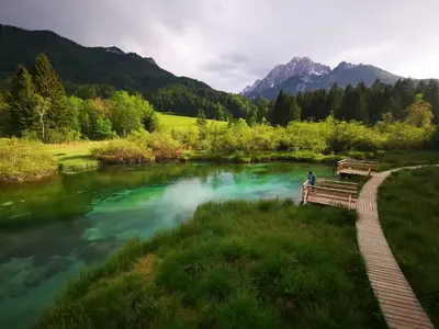 a person sitting on a bench next to a river at Hiša 109 in Kranjska Gora