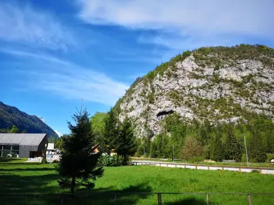 a mountain with a house and a green field at Apartma Pika in Mojstrana
