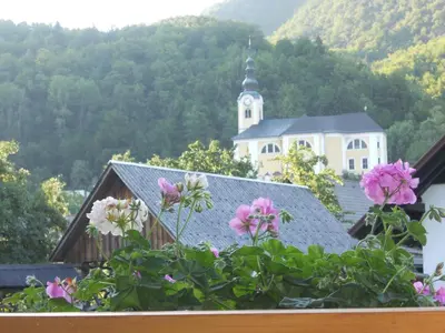 a building with a clock tower in the distance with flowers at APARTMA BREMEC-STUDIO in Bohinj