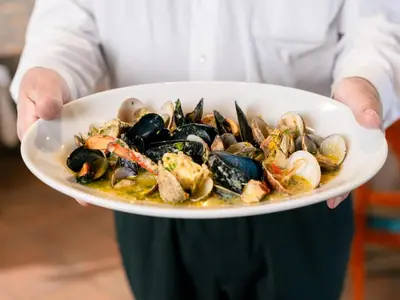 a chef holding a plate of mussels and seafood at Bužinel Estate in Dobrovo