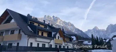 a building in front of a mountain with snow at Villa Mojca - Apartment Peridot in the Center with Private Indoor Parking in Kranjska Gora