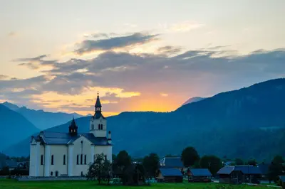 a church in a field with the sunset in the background at Apartment Ana in Bohinj