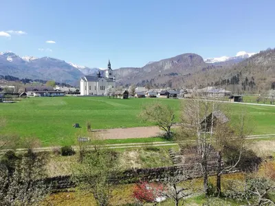 a large field with a church and mountains in the background at Apartment Ana in Bohinj