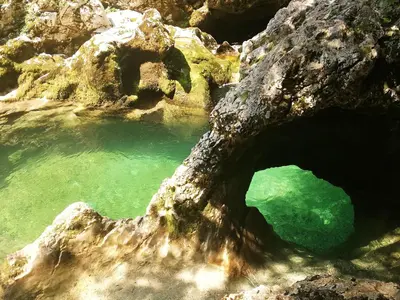 a rock cave with a green body of water at Apartment Ana in Bohinj