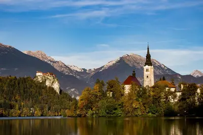 a church on the shore of a lake with mountains at APARTMA PR TAVČARJU in Zgornje Gorje