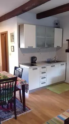 a kitchen with white cabinets and a table and a dining room at Apartmaji pri Živcovih in Dutovlje