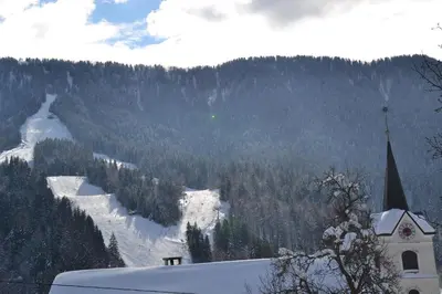 a church in the snow next to a mountain at Apartments Kot'č in Kranjska Gora