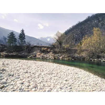 a river with rocks and trees and mountains in the background at River View Apartments Irena in Bohinj