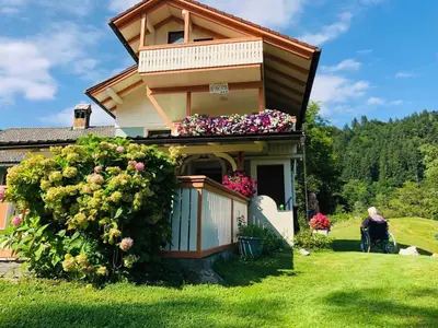 a woman sitting in a chair in front of a house with flowers at Apartma Eržen in Zgornje Gorje