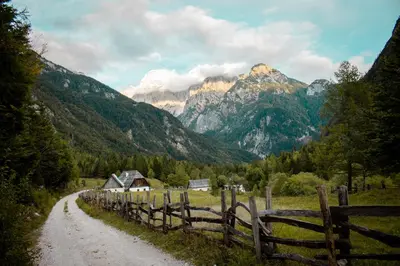 a dirt road with a fence and mountains in the background at Cottage Trenta in Bovec